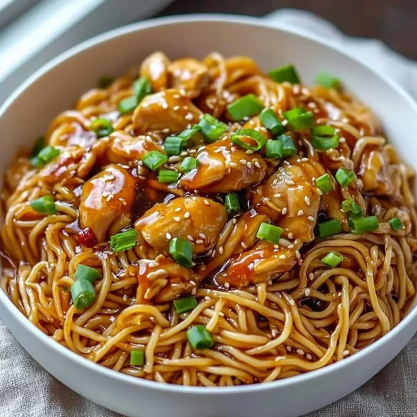 Delicious sticky garlic chicken noodles served in a bowl with fresh vegetables