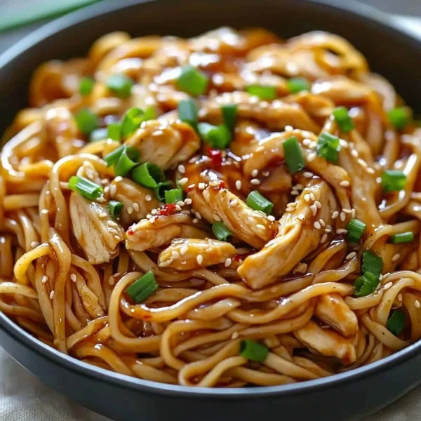 Sticky garlic chicken noodles served in a bowl with fresh herbs and vegetables.