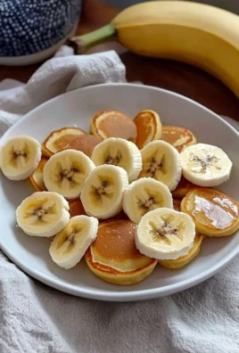 Fluffy banana mini pancakes stacked on a plate, drizzled with syrup.