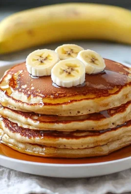 Fluffy homemade banana pancakes stacked with syrup and fresh bananas